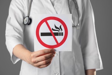 Doctor holding card with no smoking sign on gray background, closeup