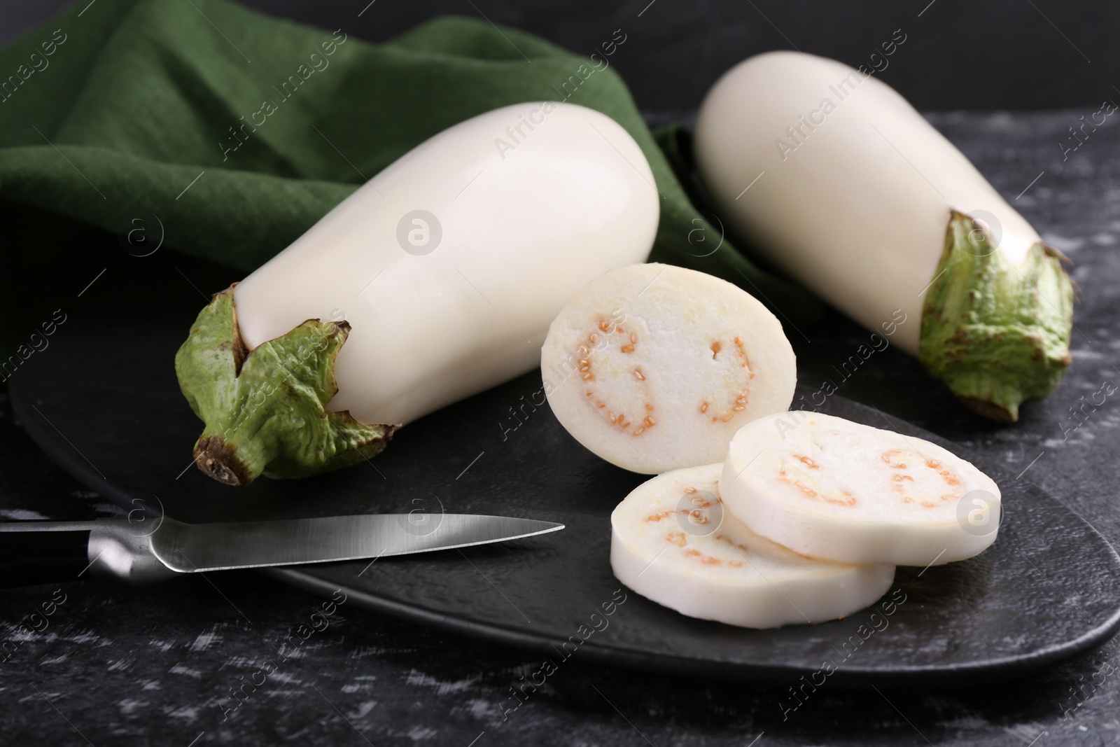 Photo of Board, raw white eggplants and knife on black textured table