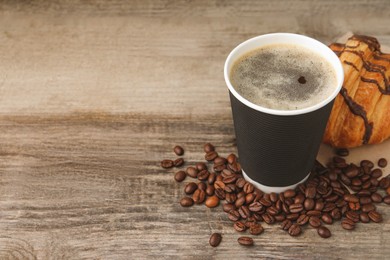 Photo of Coffee to go. Paper cup with tasty drink, croissant and beans on wooden table. Space for text