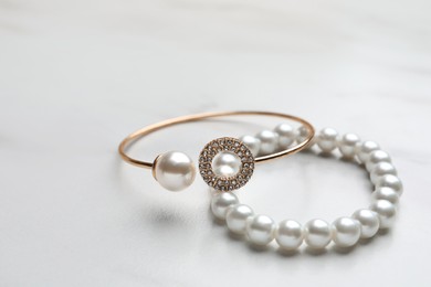 Photo of Elegant bracelets with pearls on white marble table, closeup