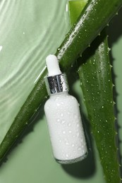 Photo of Bottle of cosmetic product and aloe leaves in water on pale green background, flat lay