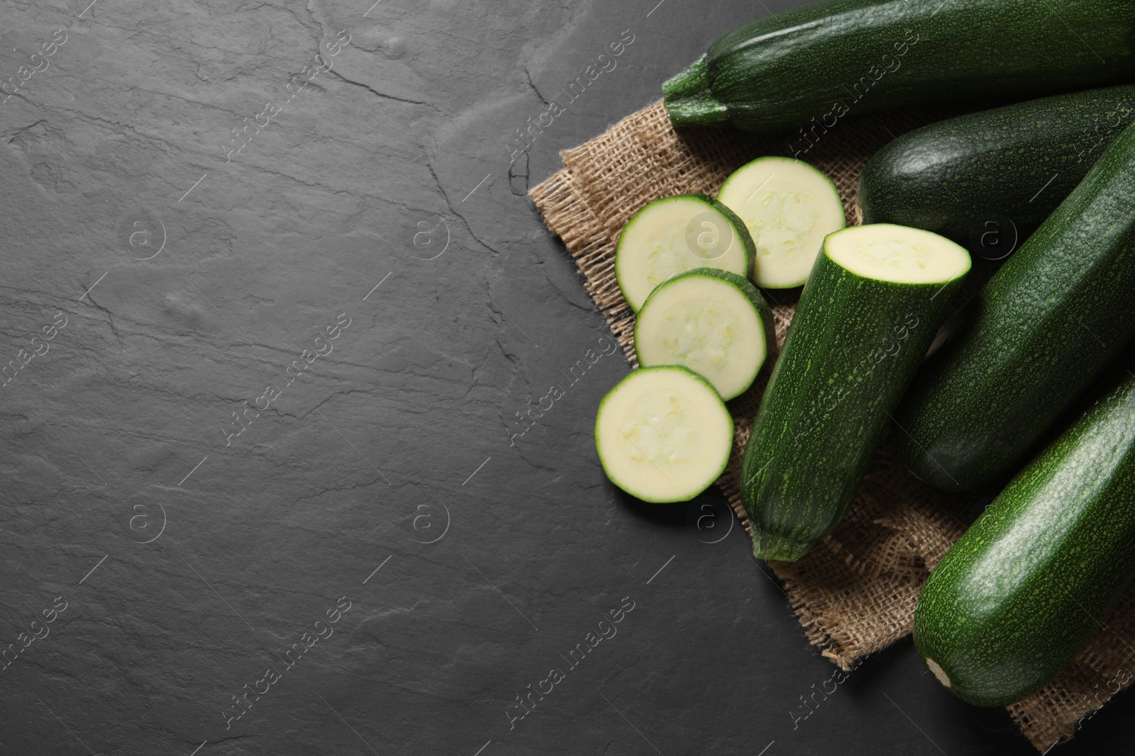 Photo of Whole and cut ripe zucchinis on black table, flat lay. Space for text