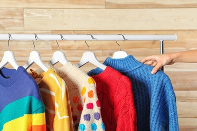 Photo of Woman choosing sweater on rack against wooden background