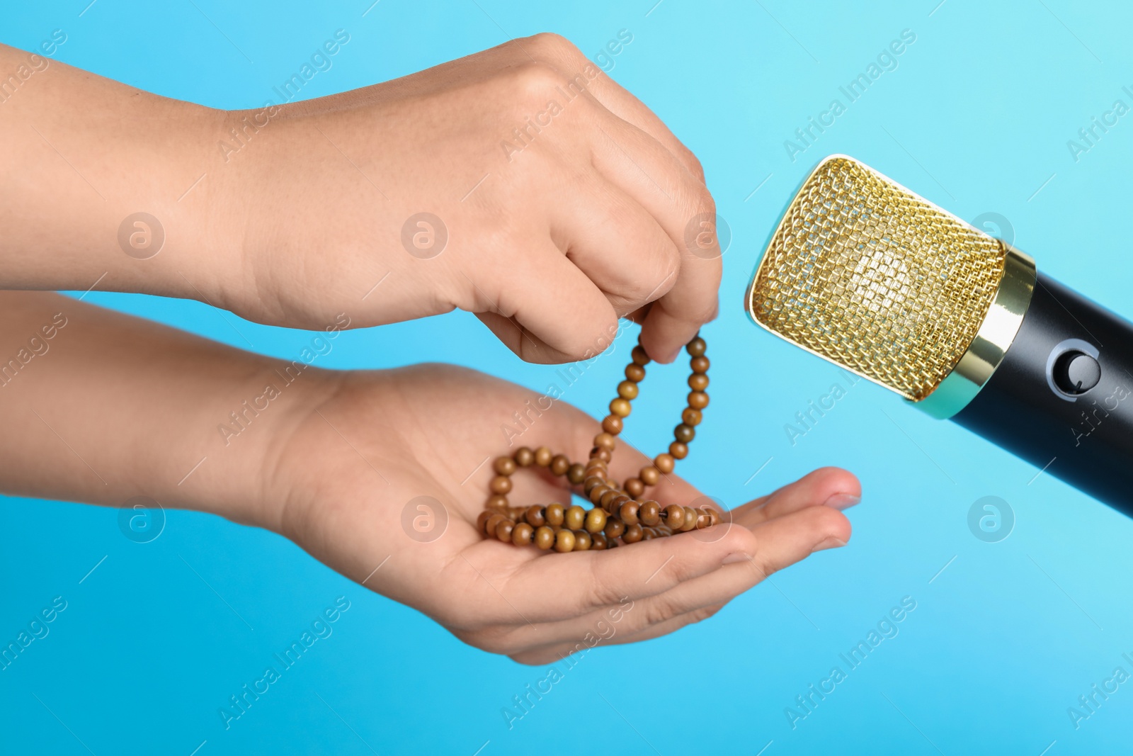 Photo of Woman making ASMR sounds with microphone and beads on light blue background, closeup