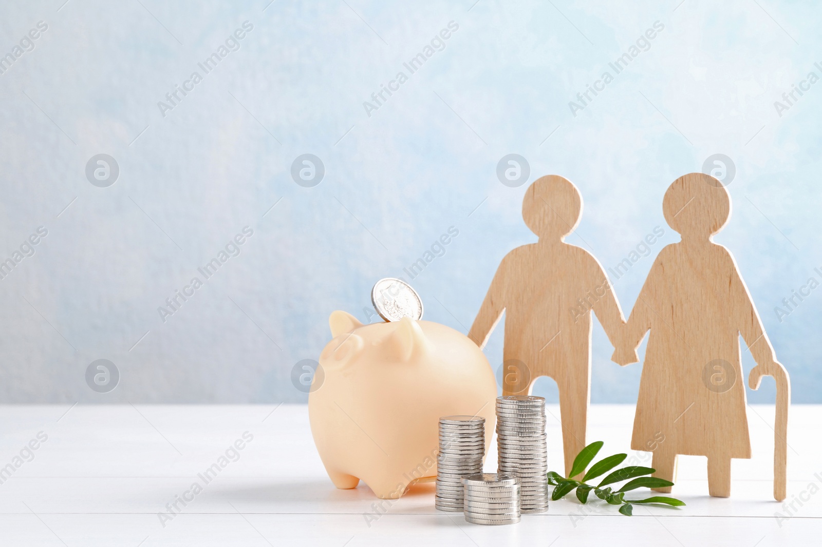 Photo of Pension savings. Figure of senior couple, stacked coins, piggy bank and green twig on white wooden table, space for text