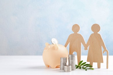 Pension savings. Figure of senior couple, stacked coins, piggy bank and green twig on white wooden table, space for text