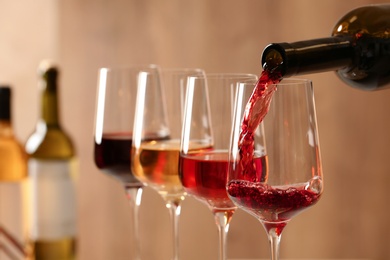 Pouring wine from bottle into glass on blurred background, closeup