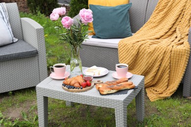 Photo of Morning drink, pastry, berries, cheese and vase with flowers on rattan table. Summer breakfast outdoors