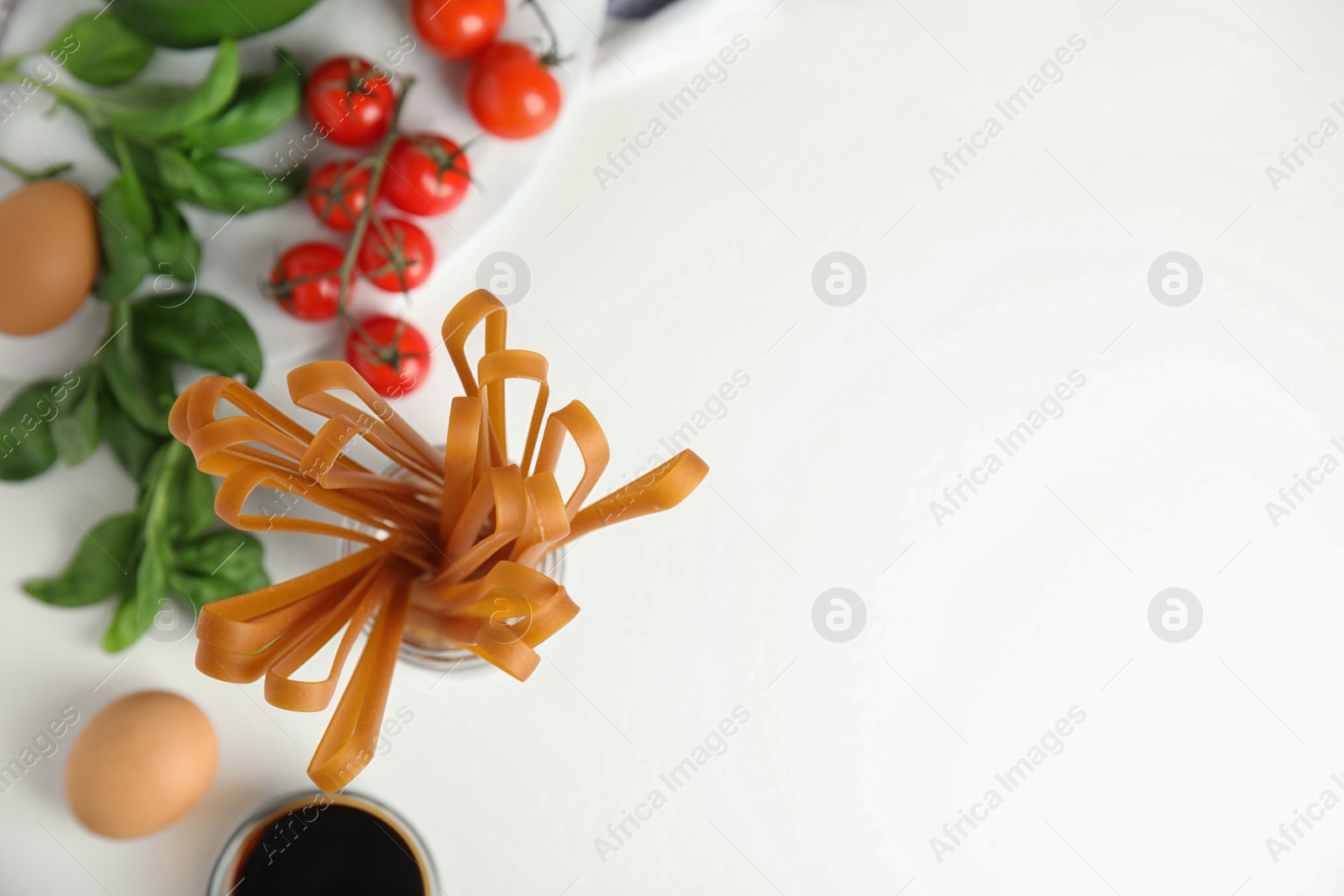 Photo of Uncooked buckwheat noodles and ingredients on white table, flat lay. Space for text