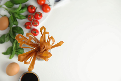 Photo of Uncooked buckwheat noodles and ingredients on white table, flat lay. Space for text