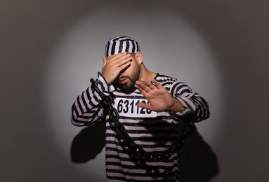 Photo of Prisoner in special uniform with chained hands on grey background