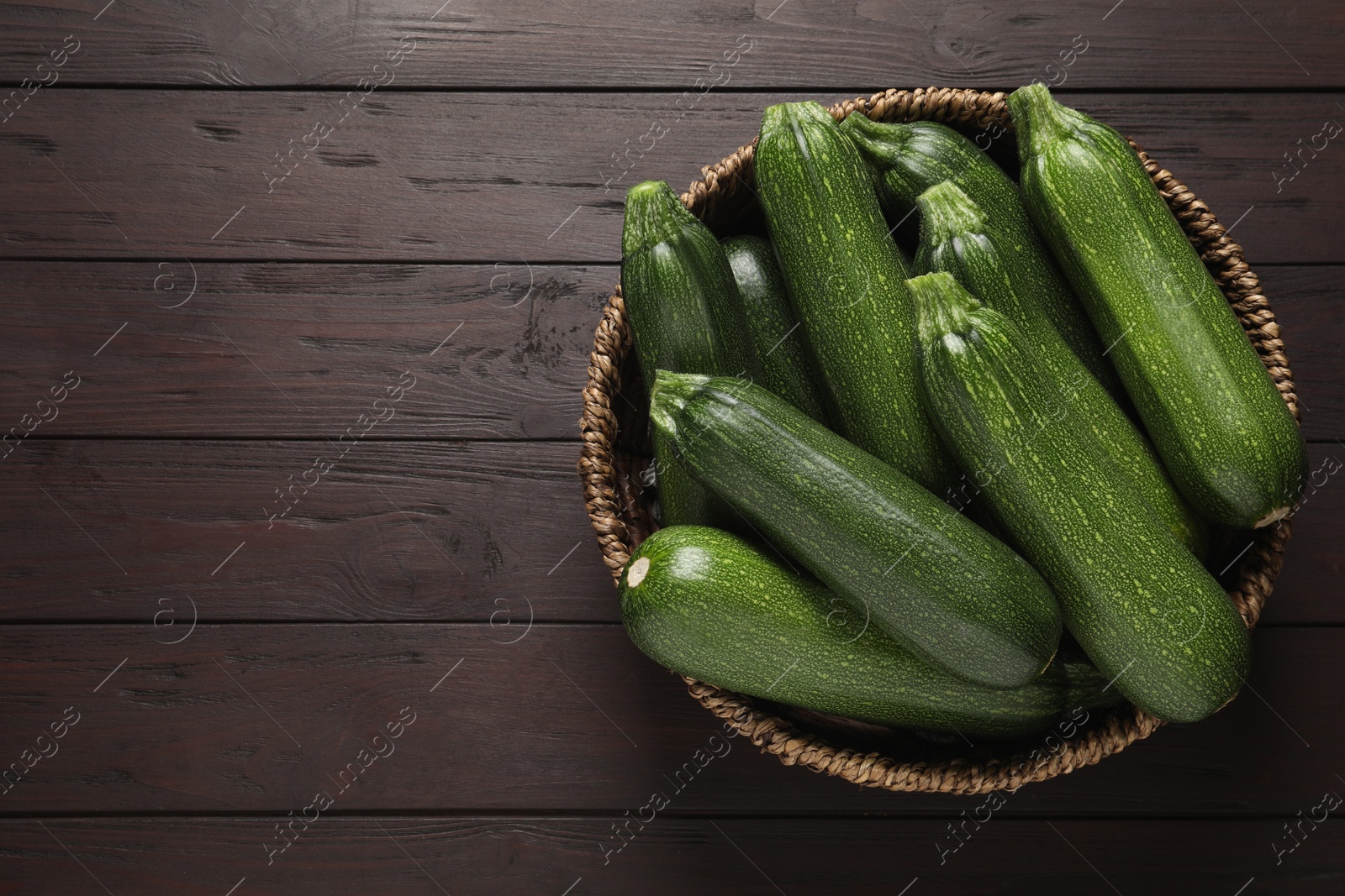 Photo of Raw ripe zucchinis in wicker bowl on wooden table, top view. Space for text