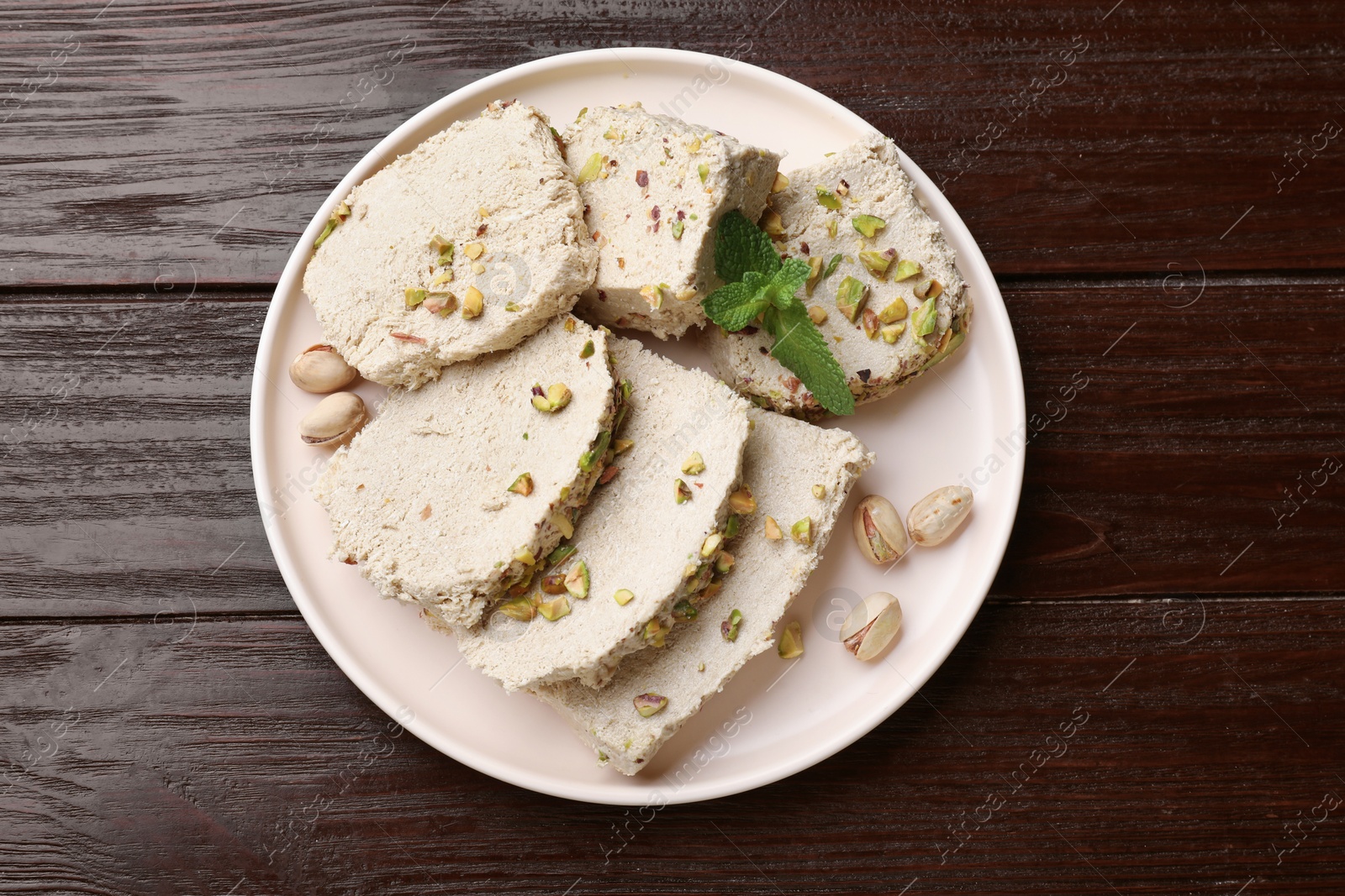 Photo of Pieces of tasty halva with pistachios and mint on wooden table, top view