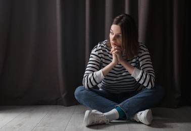 Sad young woman sitting on floor indoors, space for text