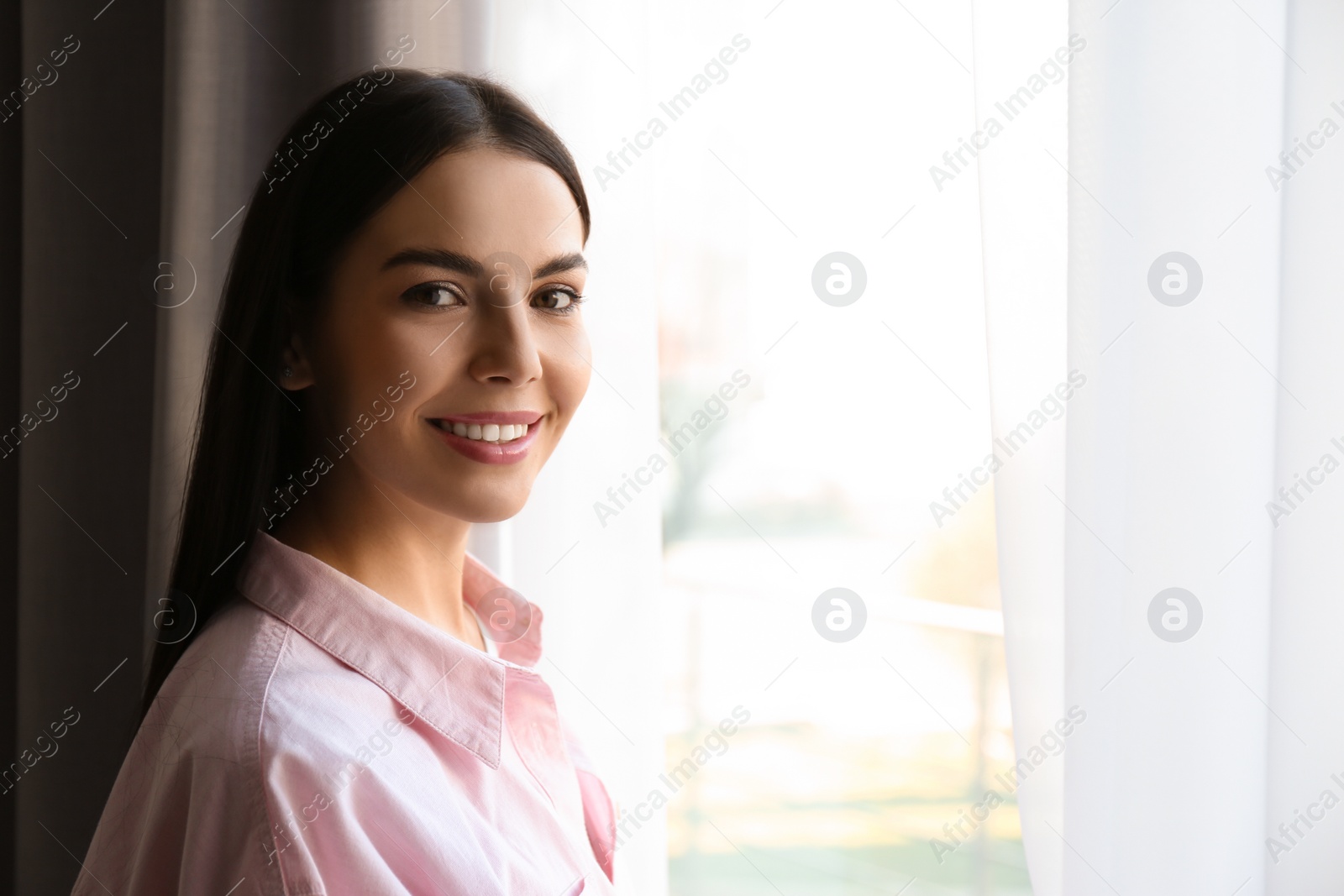 Photo of Woman near window with beautiful curtains at home. Space for text