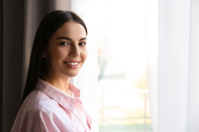 Photo of Woman near window with beautiful curtains at home. Space for text