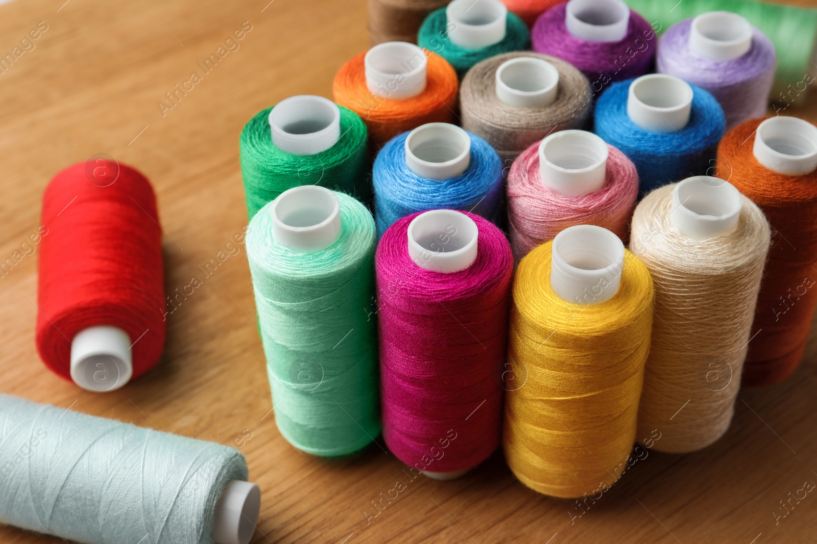 Photo of Many colorful sewing threads on wooden table