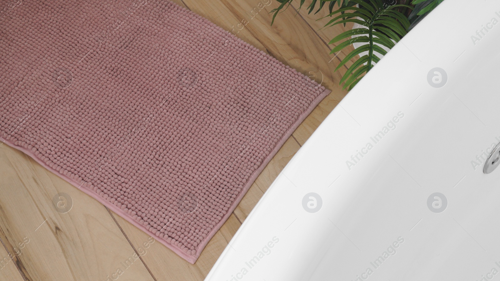 Photo of Pink mat near tub on wooden floor in bathroom, above view