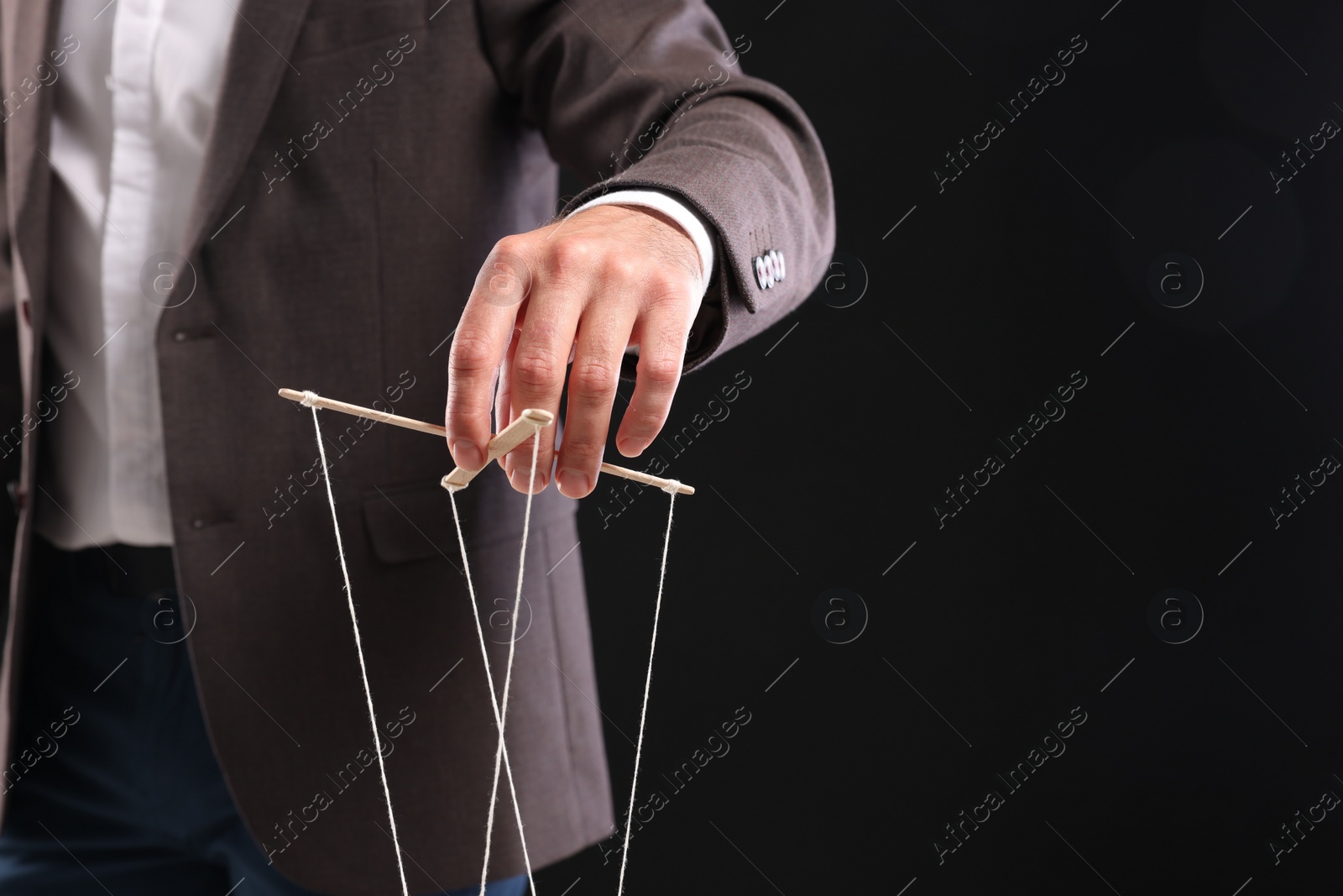 Photo of Man in suit pulling strings of puppet on black background, closeup. Space for text