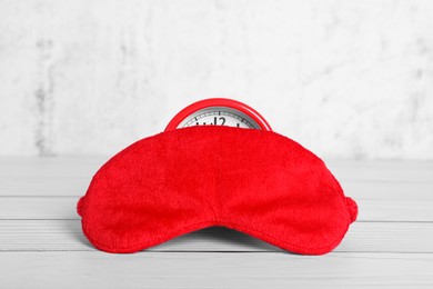 Red sleep mask and alarm clock on white wooden table