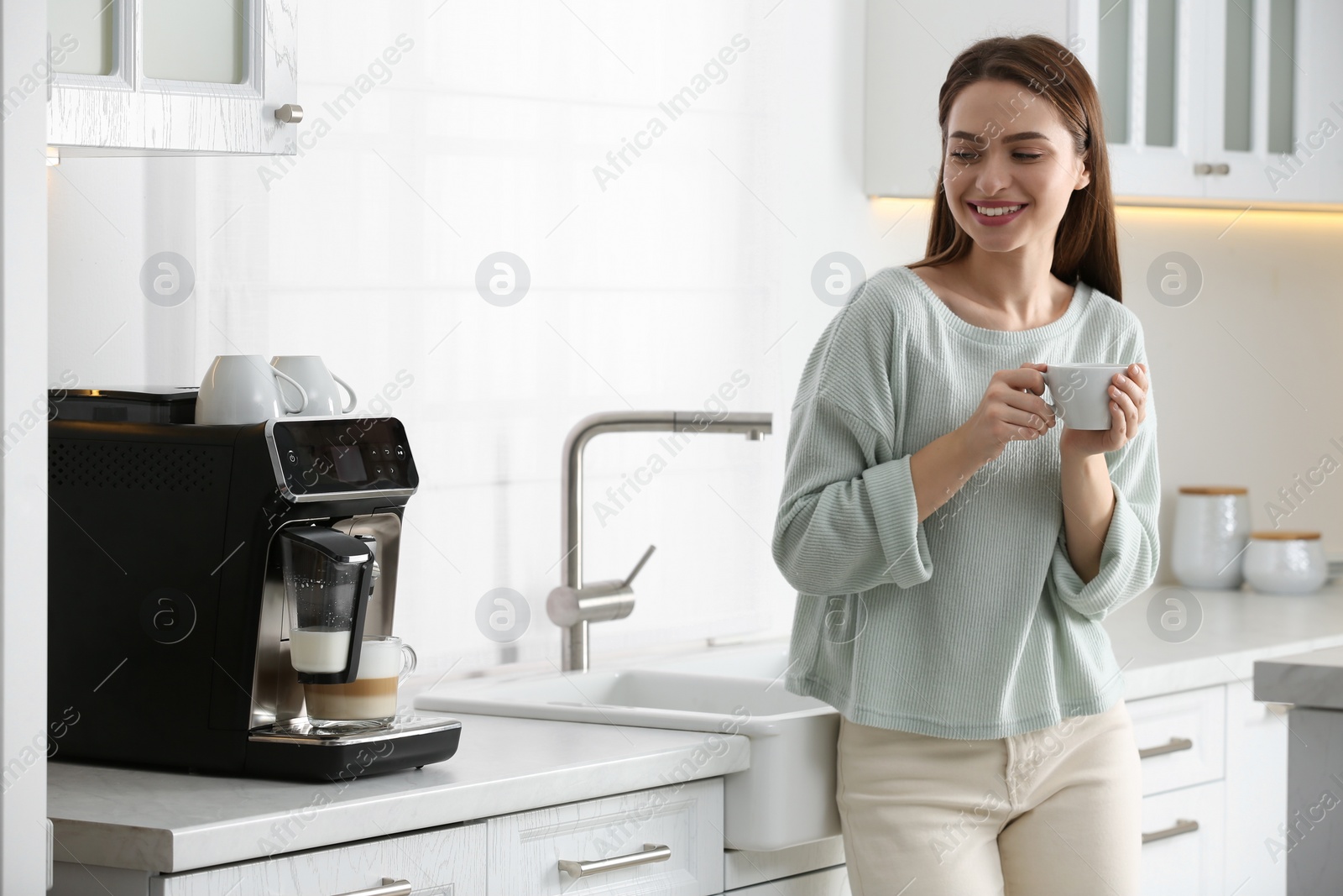 Photo of Young woman enjoying fresh aromatic coffee near modern machine in kitchen