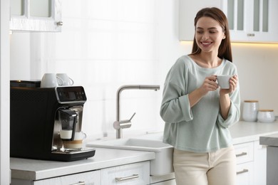 Young woman enjoying fresh aromatic coffee near modern machine in kitchen