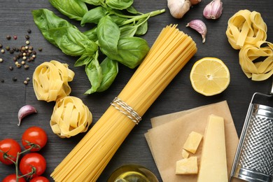 Photo of Different types of pasta, products, peppercorns and garter on dark wooden table, flat lay