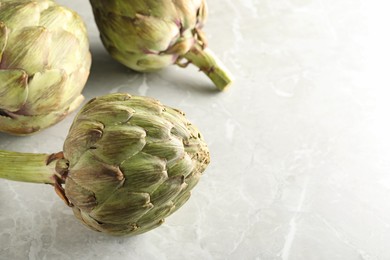 Fresh raw artichokes on grey marble table. Space for text