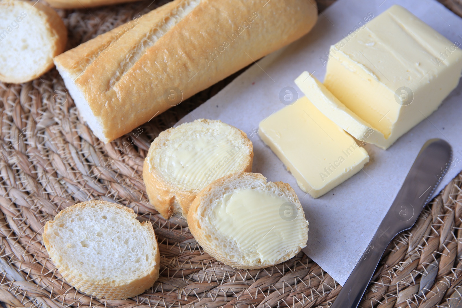 Photo of Tasty cut baguette with fresh butter on wicker mat