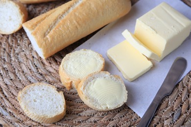 Photo of Tasty cut baguette with fresh butter on wicker mat