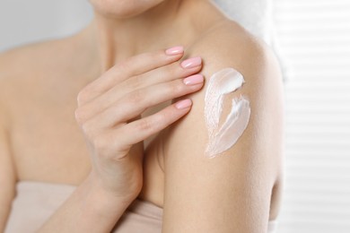 Woman applying body cream onto shoulder on blurred background, closeup