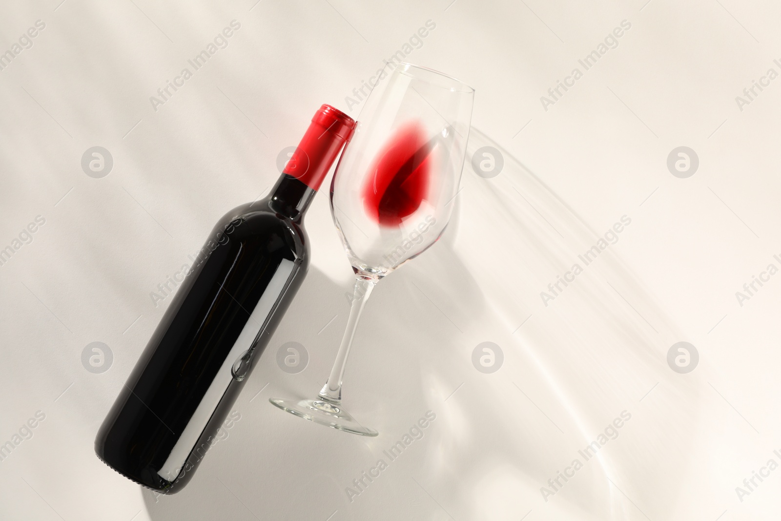 Photo of Bottle of expensive red wine and wineglass on light background, top view. Space for text