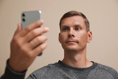 Man unlocking smartphone with facial scanner on beige background. Biometric verification