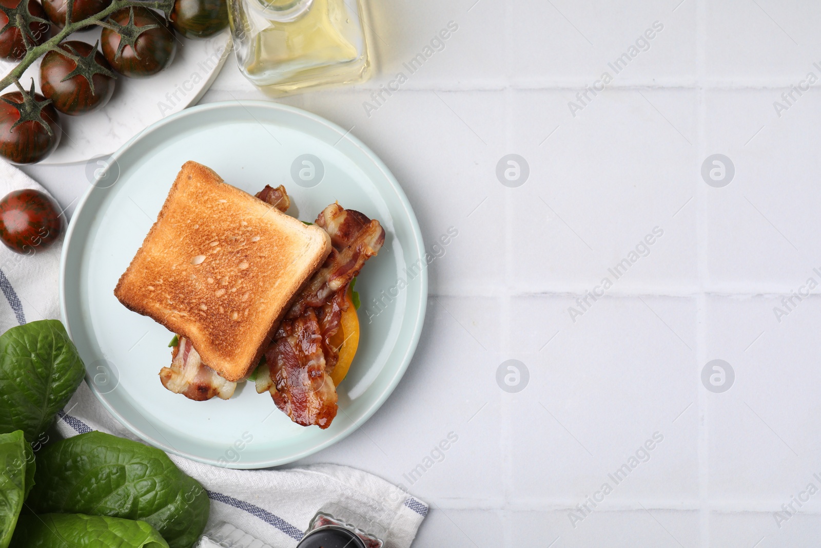 Photo of Tasty sandwich with bacon, tomatoes and spices on white tiled table, flat lay. Space for text