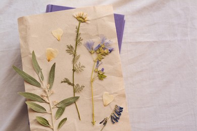 Photo of Sheet of paper with dried flowers and leaves on white fabric, top view. Space for text