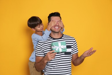 Photo of Man receiving gift for Father's Day from his son on yellow background