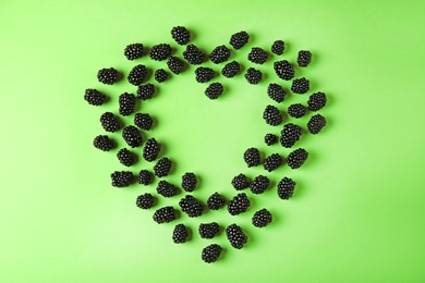 Heart shaped frame made of tasty blackberries on green background, top view with space for text