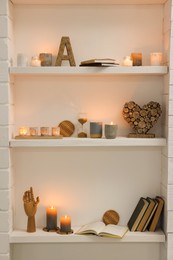 Photo of Burning wax candles and different decor on shelves