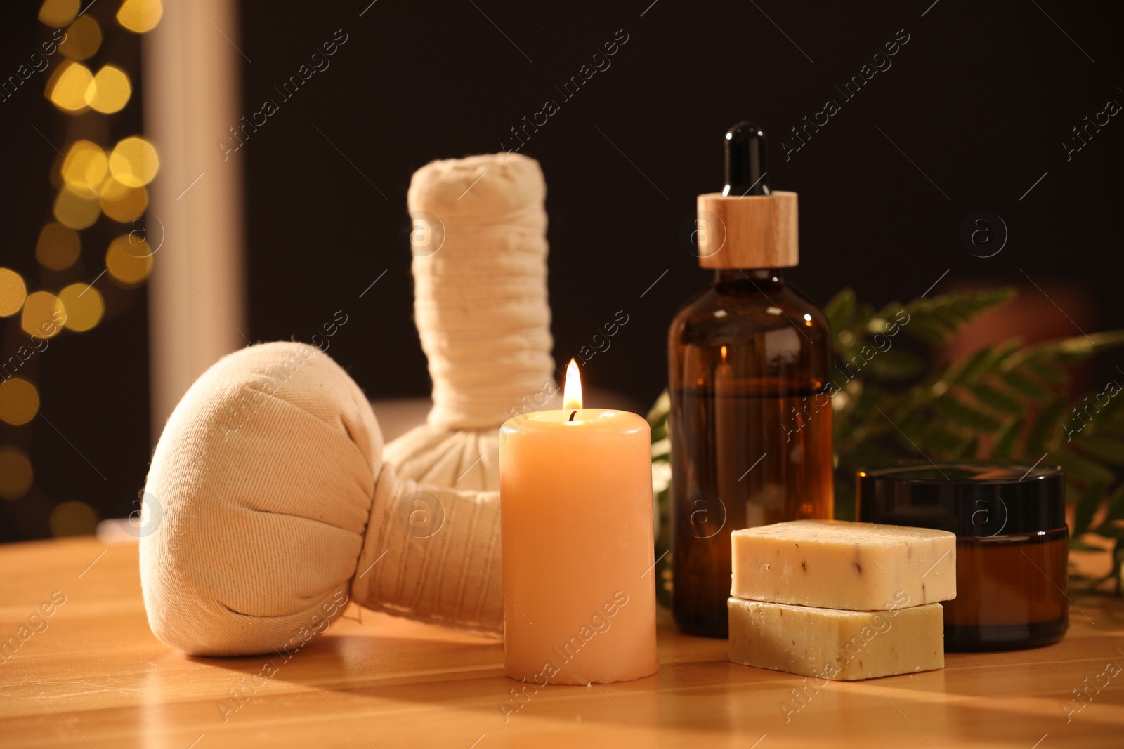 Photo of Spa composition. Cosmetic products, herbal bags and burning candle on wooden table