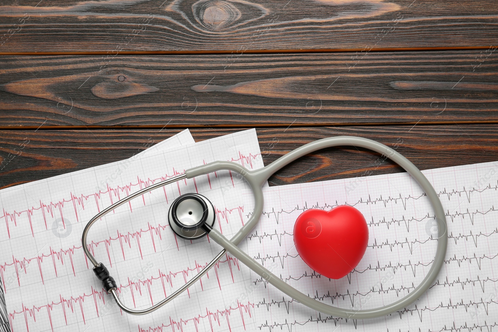 Photo of Stethoscope, red heart and cardiogram on wooden table, flat lay with space for text. Cardiology concept