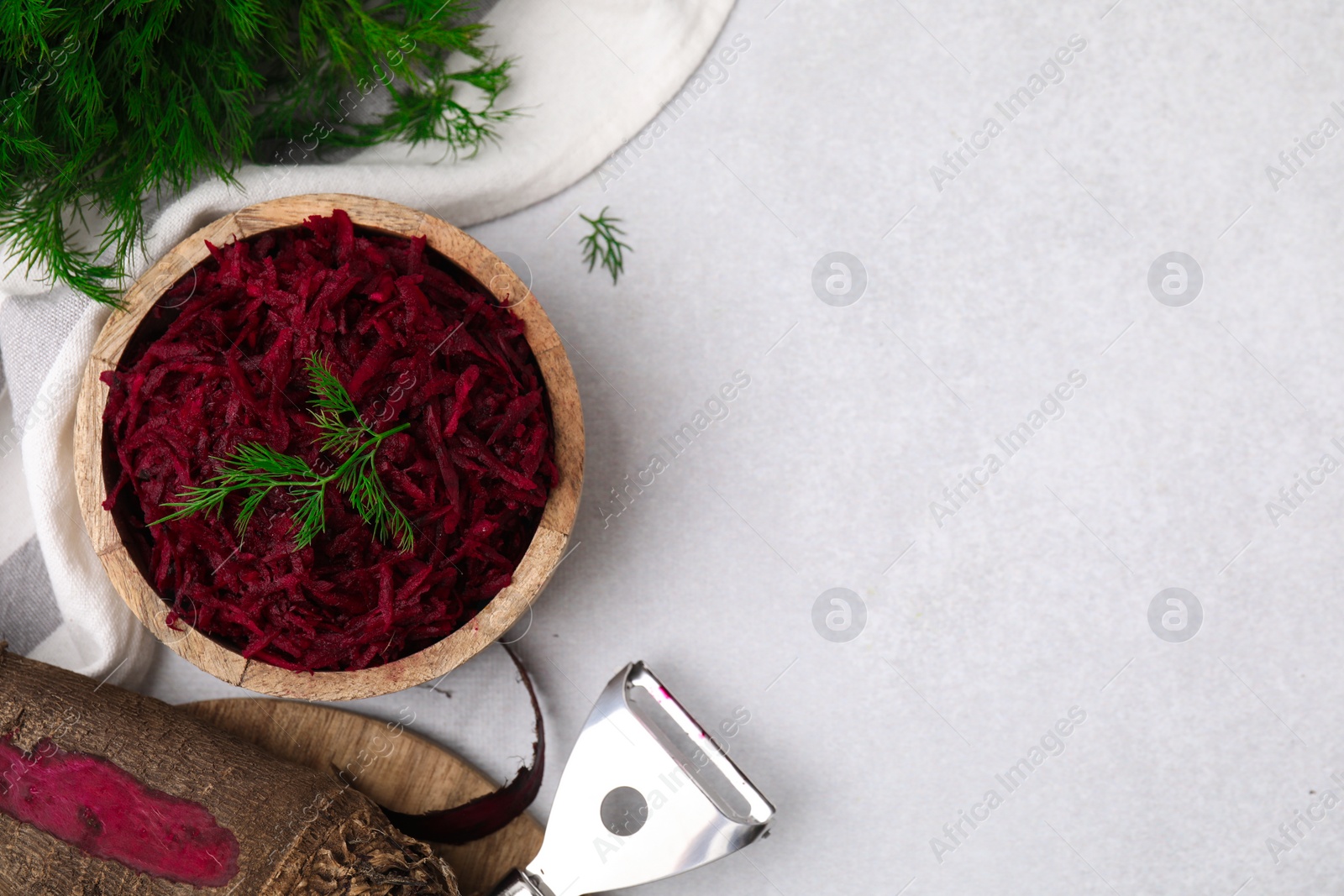 Photo of Grated red beet with dill in bowl and vegetable peeler on light gray table, flat lay. Space for text