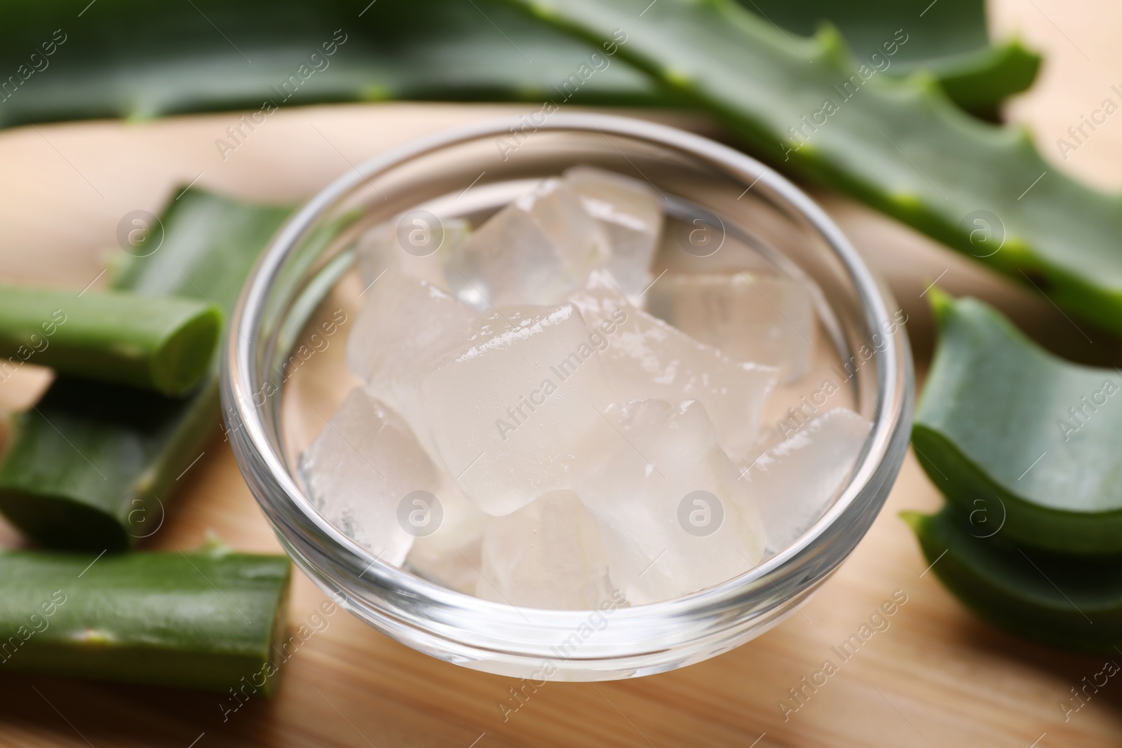 Photo of Aloe vera gel and slices of plant on wooden table, closeup