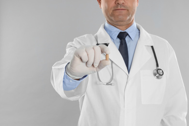 Doctor holding suppository for hemorrhoid treatment on light grey background, closeup
