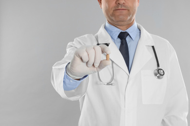 Photo of Doctor holding suppository for hemorrhoid treatment on light grey background, closeup