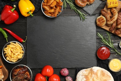 Photo of Flat lay composition with barbecued meat and vegetables on black wooden table. Space for text