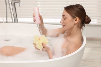 Photo of Woman pouring shower gel onto mesh pouf in bath indoors