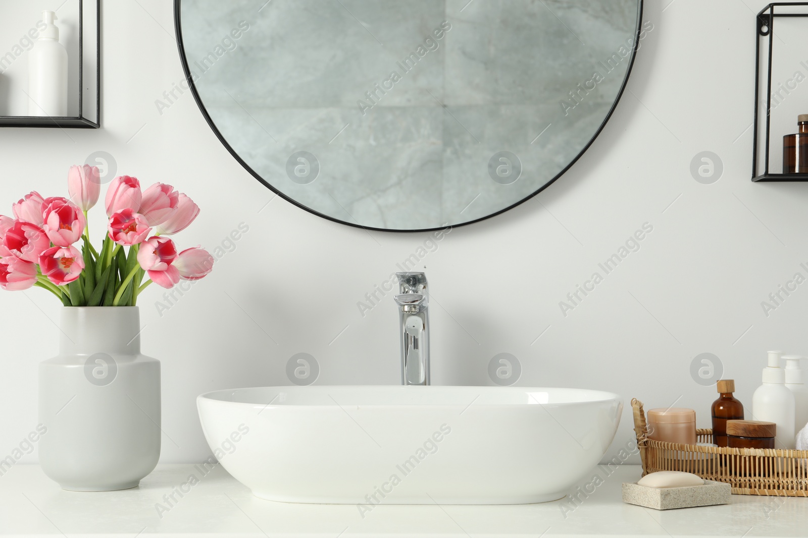 Photo of Vase with beautiful pink tulips and toiletries near sink in bathroom