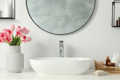 Vase with beautiful pink tulips and toiletries near sink in bathroom