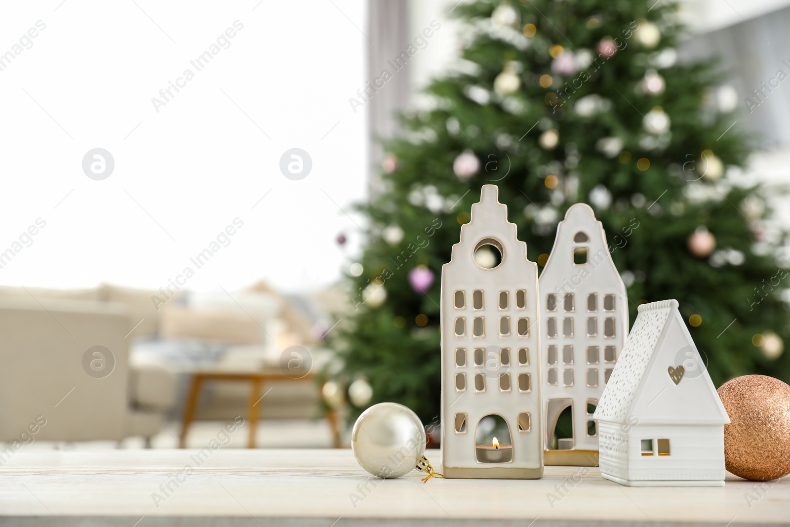 Photo of Beautiful house shaped candle holders and baubles on table indoors, space for text. Bokeh effect