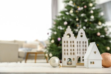 Photo of Beautiful house shaped candle holders and baubles on table indoors, space for text. Bokeh effect